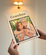 A personalized hardcover book titled 'Grandma' is held by two hands against a warm, softly lit cream-colored paneled wall. The book cover features a custom illustration of a grandmother and granddaughter hugging, framed by a dark navy border.